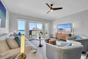 En moderne stue med balkon, loftventilator, fladskærms-tv og udsigt til stranden.
