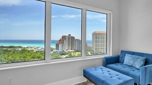 A room with a large window offering a view of the ocean and buildings. - Sandy Shores Escape · Stunning beach views  *Not your grandma’s condo* (Miramar Beach)
