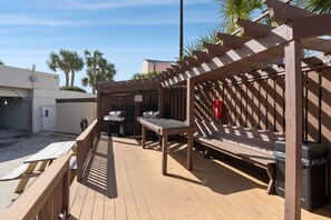 A wooden deck with a barbecue area, a bench, and a trash can. - Sandy Shores Escape · Stunning beach views  *Not your grandma’s condo* (Miramar Beach)