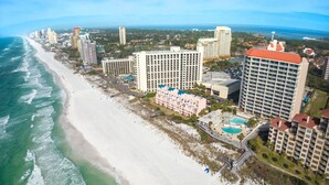 An aerial view of a coastal hotel area with beachfront properties, a swimming pool, and a beach. - Sandy Shores Escape · Stunning beach views  *Not your grandma’s condo* (Miramar Beach)