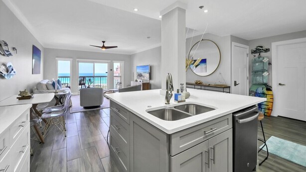 A modern kitchen with a large island, white cabinetry, and a view to the outside. - Sandy Shores Escape · Stunning beach views  *Not your grandma’s condo* (Miramar Beach)