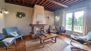 Una sala de estar acogedora con chimenea de piedra, vigas de madera en el techo y vistas al exterior a través de un ventanal grande.