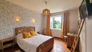 Un dormitorio con una cama de madera, dos mesitas de noche, un televisor en la pared y una ventana con cortinas.