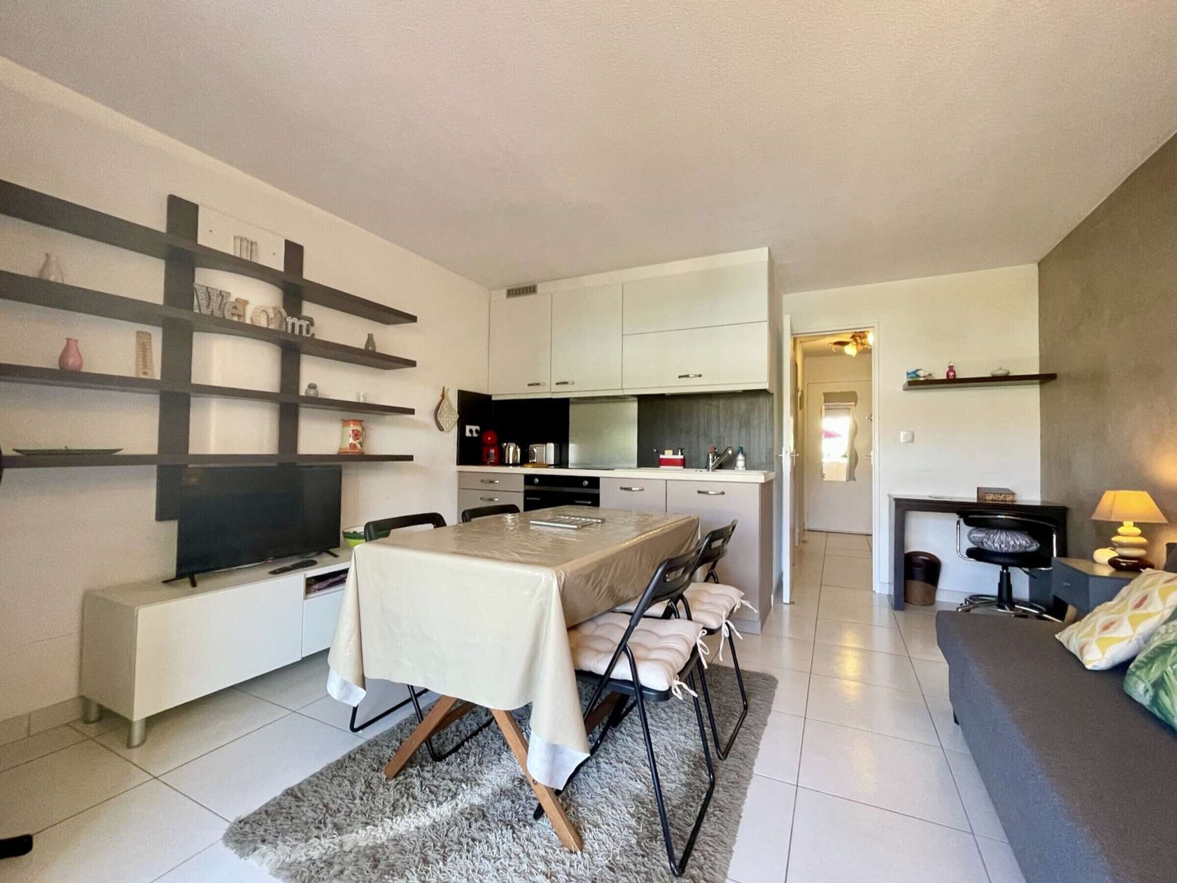 Un salon moderne et bien éclairé, comprenant un coin repas, une cuisine et un petit espace détente avec un canapé et une table.