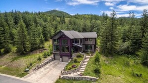 A two-story house with a dark exterior, surrounded by a forested area and a mountain in the background. - Private chalet on golf course 5 min to Silver mntn (Kellogg)