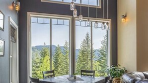 A dining area with a checkered floor, a round table, and chairs. There are large windows with a view of trees and mountains. - Private chalet on golf course 5 min to Silver mntn (Kellogg)