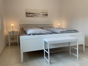 Une chambre à coucher moderne avec un lit blanc, deux lampes de chevet, une table de chevet et un tableau accroché au mur.