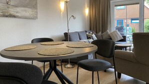 Una sala de estar moderna con una mesa de comedor redonda, sillas negras, un sofá gris y un ventanal con cortinas.