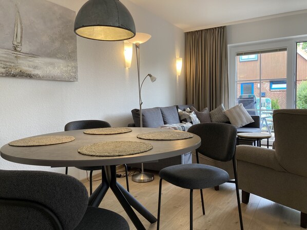Un salon moderne avec une table à manger ronde, des chaises noires, un canapé gris et une grande fenêtre avec des rideaux.