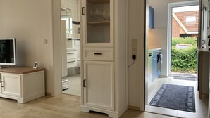 Una cocina moderna con armarios blancos, horno empotrado y vista a una casa de ladrillo a través de la puerta abierta.