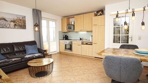 A modern kitchen with wooden cabinets, a dining table, and a gray chair. - Die Ferienwohnung Austernperle im Haus am Kurpark in Baabe (Baabe)