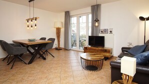 A modern living room with a dining table, chairs, a sofa, a TV, and a fireplace. - Die Ferienwohnung Austernperle im Haus am Kurpark in Baabe (Baabe)