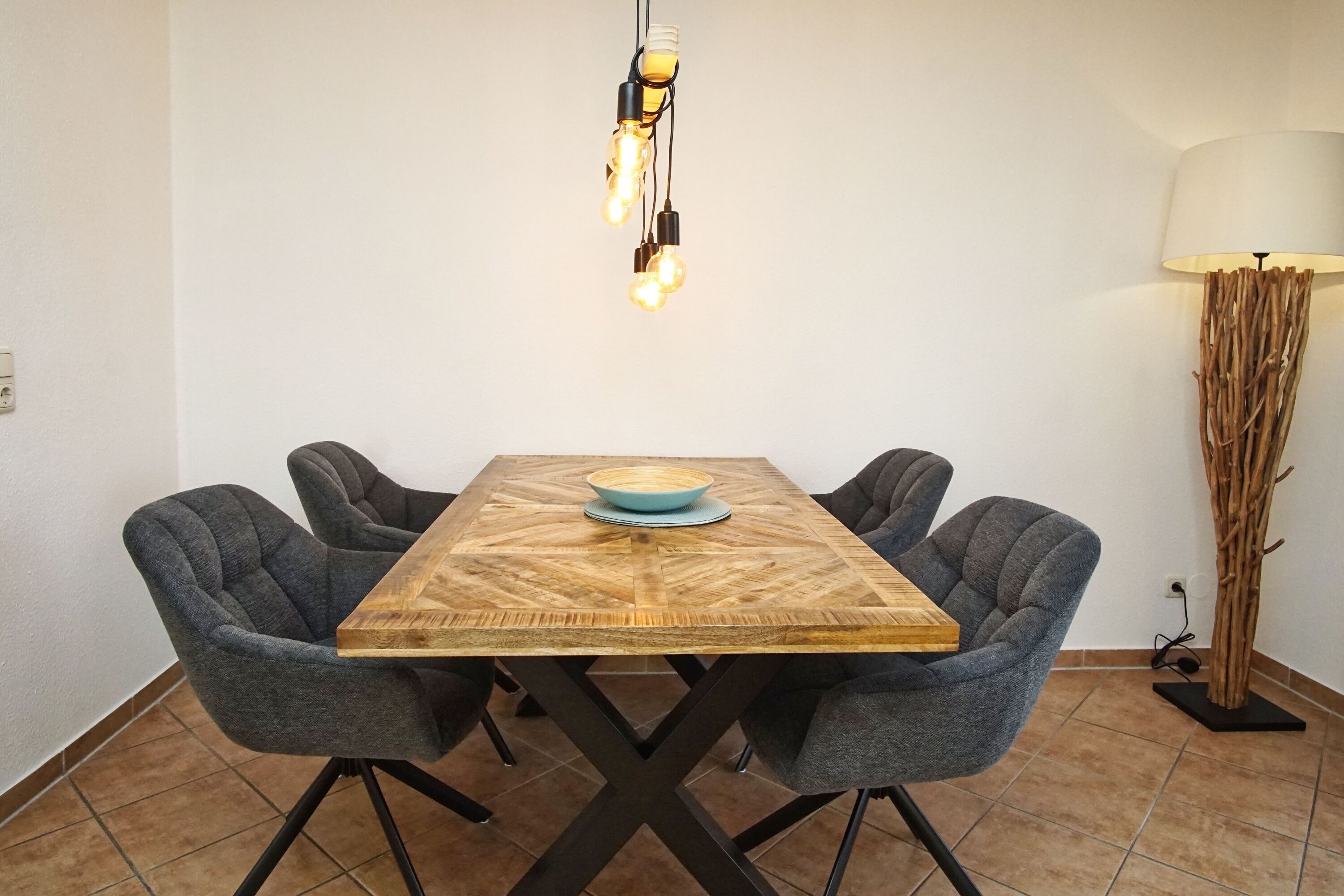 A dining table with four chairs, a bowl, and a hanging light fixture.