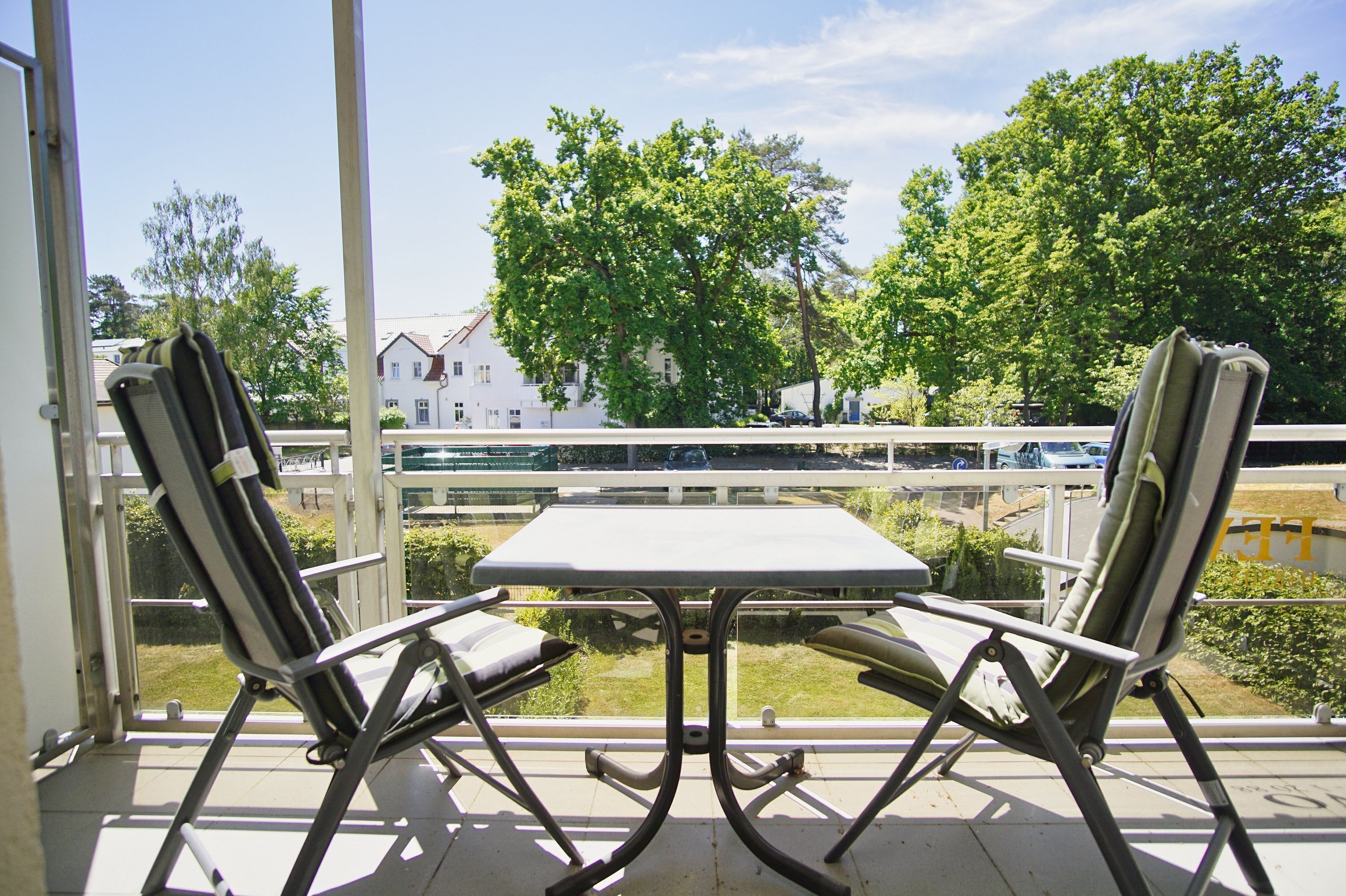 A balcony with two chairs and a table, overlooking a street with cars and trees.