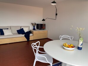 A modern living room with a sofa, a dining table with chairs, a TV, and a vase with flowers.
