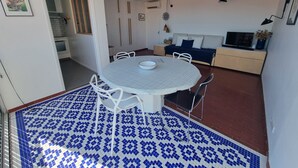 A dining area with a round table and chairs, a sofa, a TV, and a patterned floor. - Charming air-conditioned T2 near sea, 4 pers (Collioure)