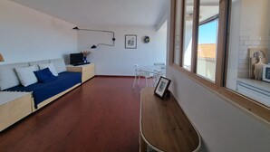 A modern living room with a sofa, a desk, a chair, and a large window. - Charming air-conditioned T2 near sea, 4 pers (Collioure)