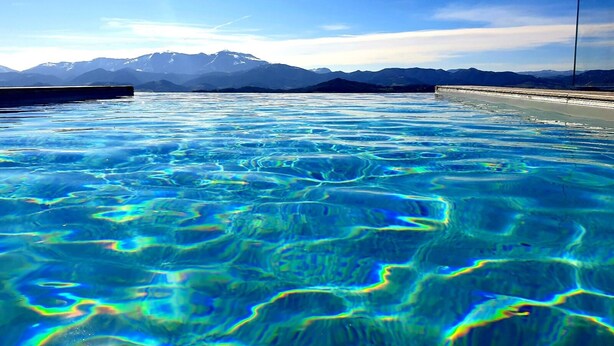 Piscina cristalina con vista a la montaña, rodeada por una terraza de hormigón.