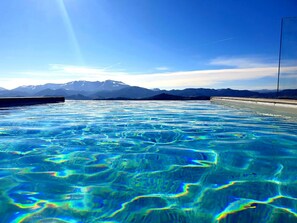 A clear pool with a mountain view, surrounded by a concrete deck. - Aura Relais (Urbino)