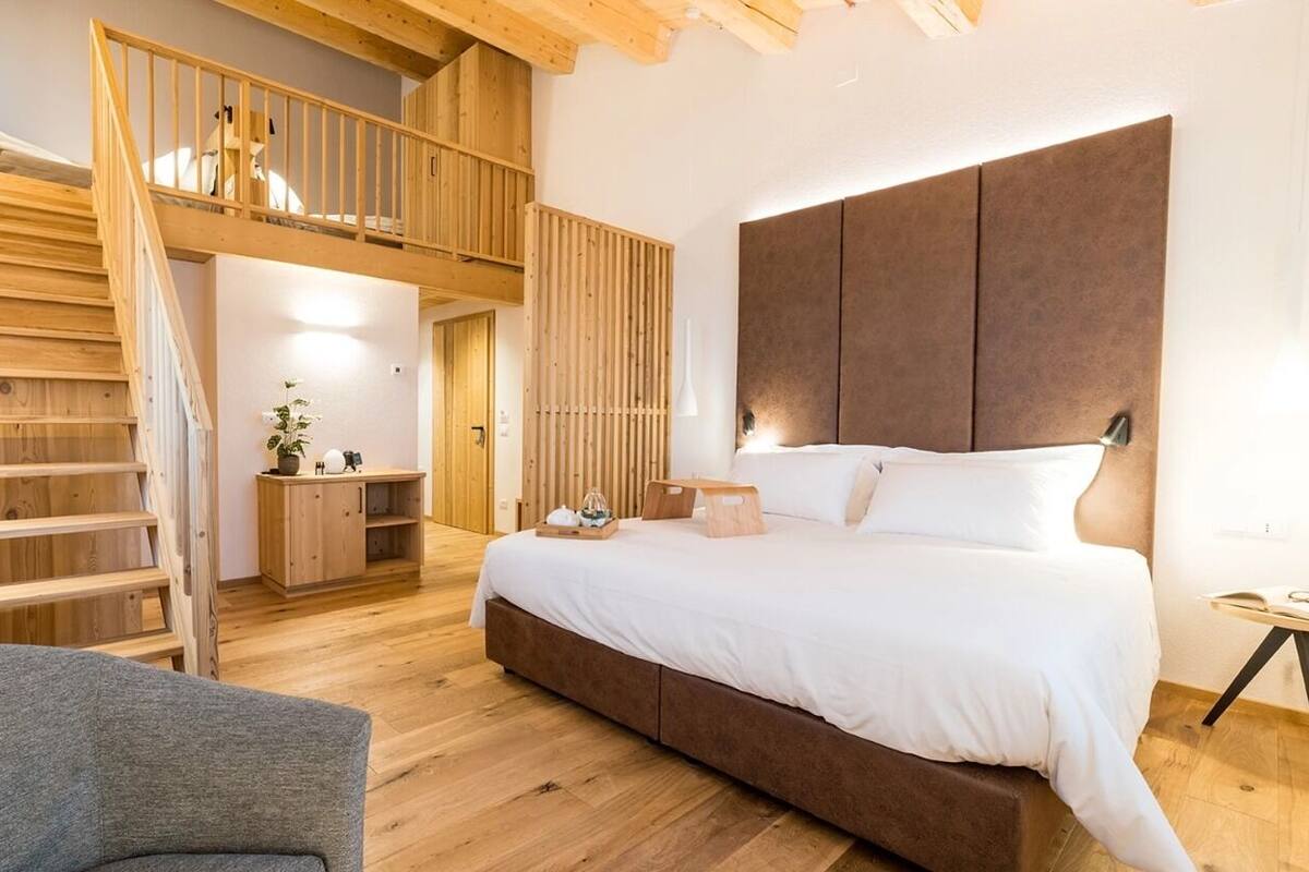 A bedroom with a wooden staircase, a bed with a headboard, a bedside table, and a chair.
