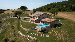 Una casa grande con piscina, rodeada de césped y árboles.