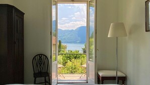 Ein Schlafzimmer mit Bett, einem Sessel, einer Lampe und Blick auf einen Balkon mit Gartenmöbeln.