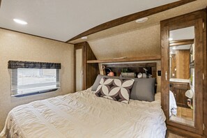 A bedroom with a large bed, a window with blinds, a mirror, and a wooden ceiling. - Chestnut Camper: Unique lodging experience! (Lancaster)