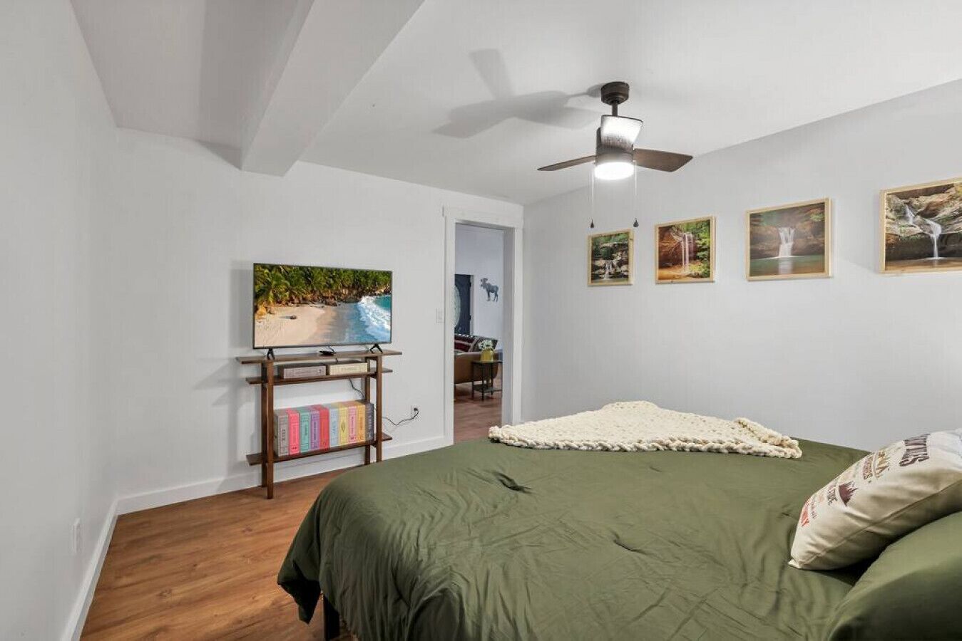 A bedroom with a bed, a ceiling fan, a TV on a stand, and framed pictures on the wall.
