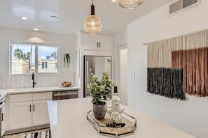 A modern kitchen with white cabinets, a stainless steel refrigerator, a dining table with a tray, and a hanging light fixture.