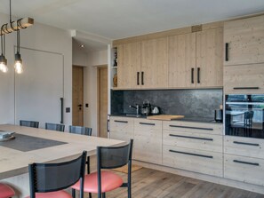 A modern kitchen with wooden cabinets, a central island, and a dining area with chairs.
