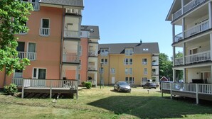 Ein mehrstöckiges Wohngebäude mit Balkonen, einem grünen Innenhof und geparkten Autos.