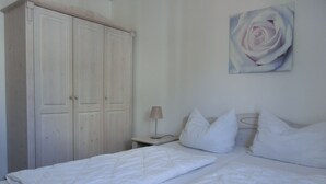 Ein Schlafzimmer mit zwei Betten, einem Kleiderschrank, einem Nachttisch, einer Lampe und einem Rosenbild.
