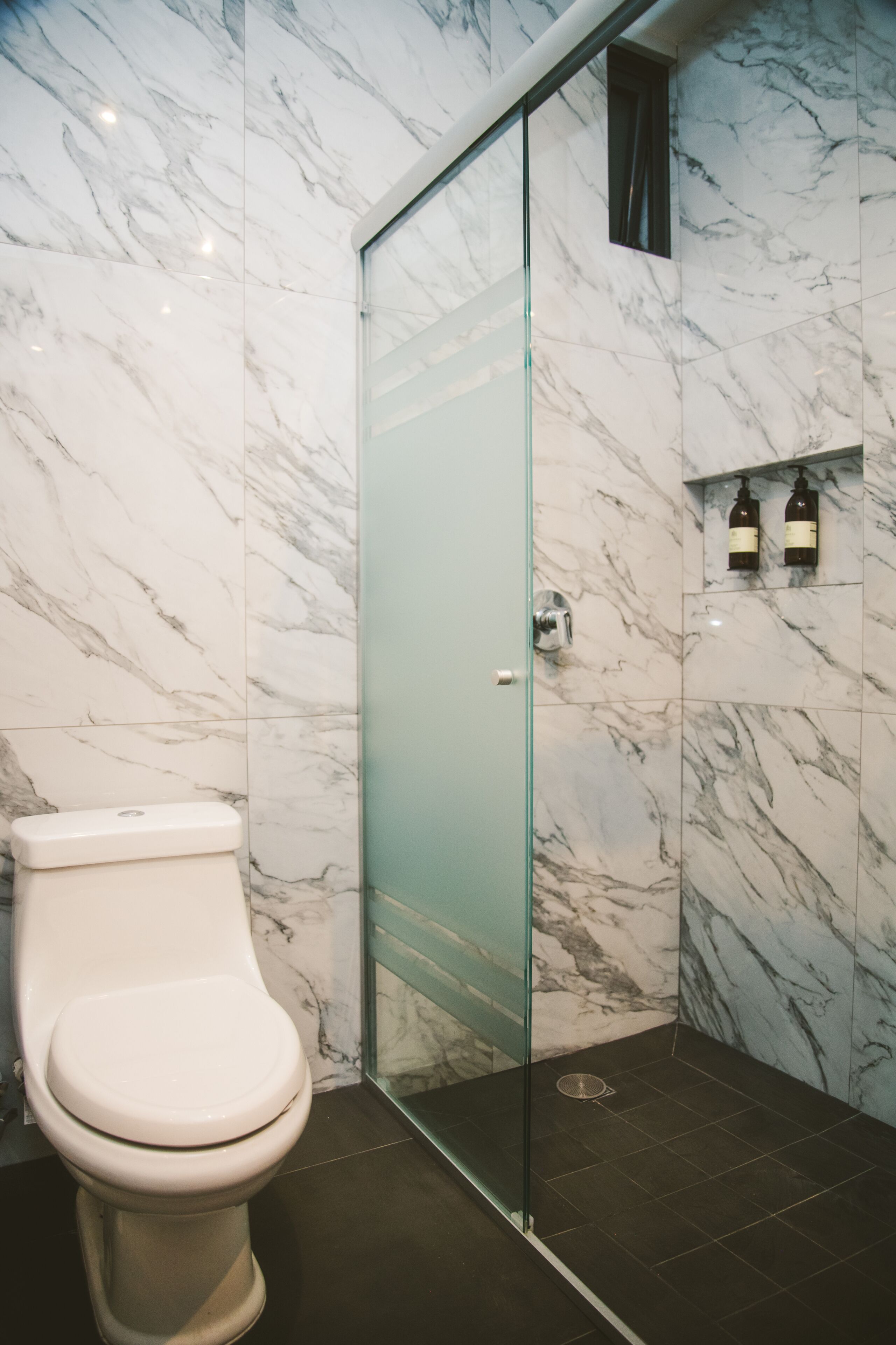 Un baño con pared de mármol, cabina de ducha de vidrio y un inodoro.