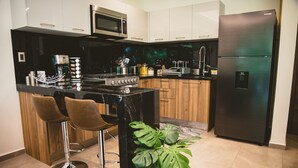 Et moderne køkken med en central ø, barstole, et rustfrit stål køleskab og en mikrobølgeovn.