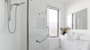 Ein modernes Badezimmer mit Duschkabine aus Glas, einem großen Fenster und einem weißen Waschtisch mit Spiegel.