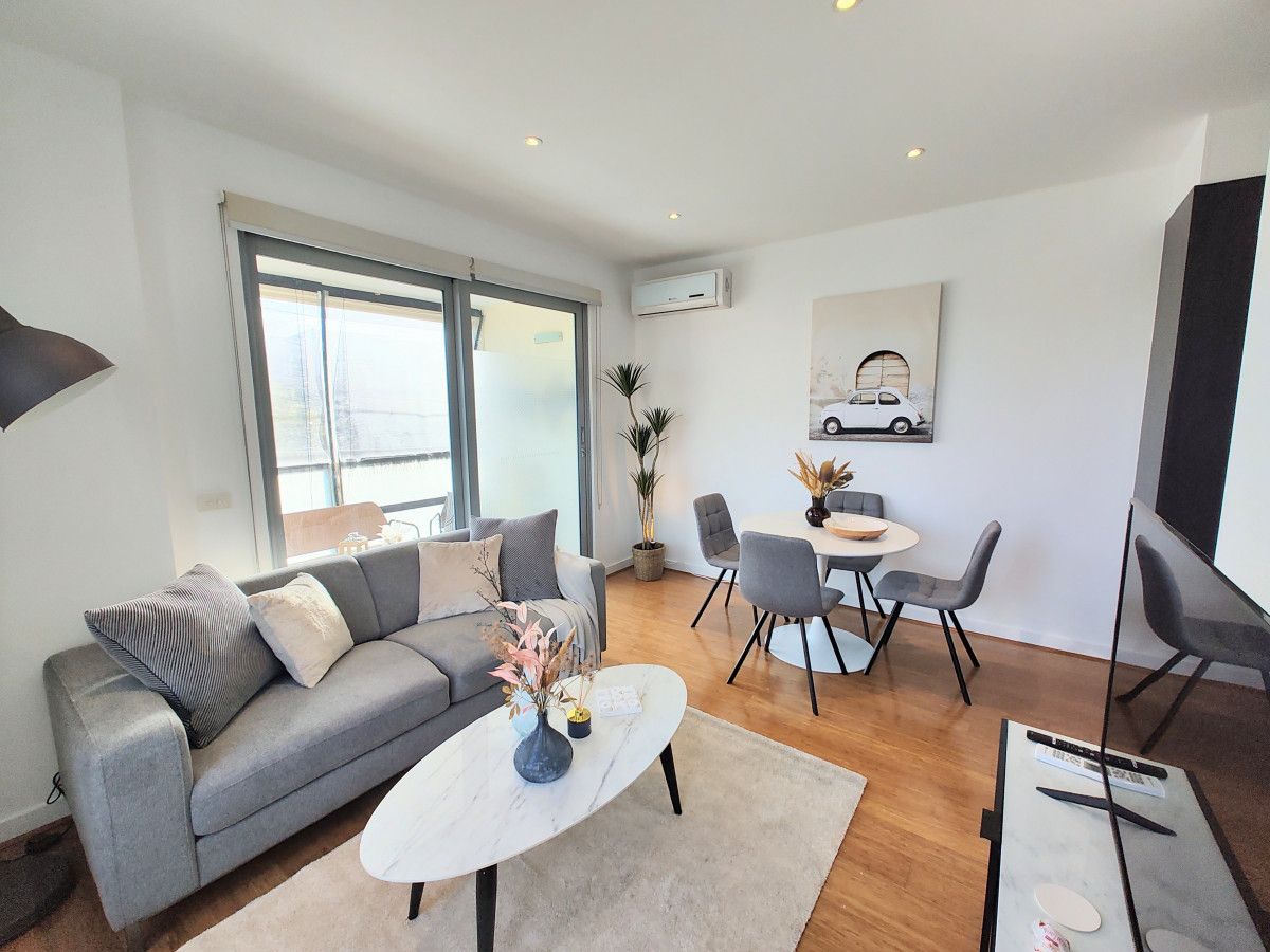 Un salon moderne avec un canapé gris, une table basse blanche et un coin repas avec des chaises grises.