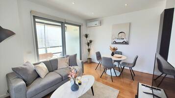A modern living room with a grey sofa, a white coffee table, and a dining area with grey chairs.