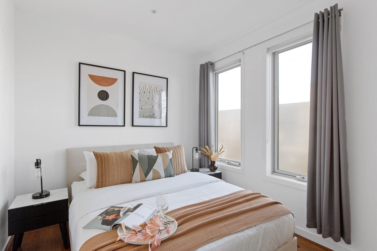 A hotel room with a bed, a nightstand, a window with curtains, and two framed artworks on the wall.