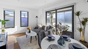 Un salon moderne avec un canapé gris, une table basse ronde et un coin repas avec une table blanche mise pour deux personnes.