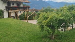 A house with a sloped roof, a balcony with red flowers, and a view of mountains.