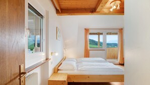 A bedroom with a wooden bed, a window with a view of the outdoors, a radiator, and a wooden ceiling.