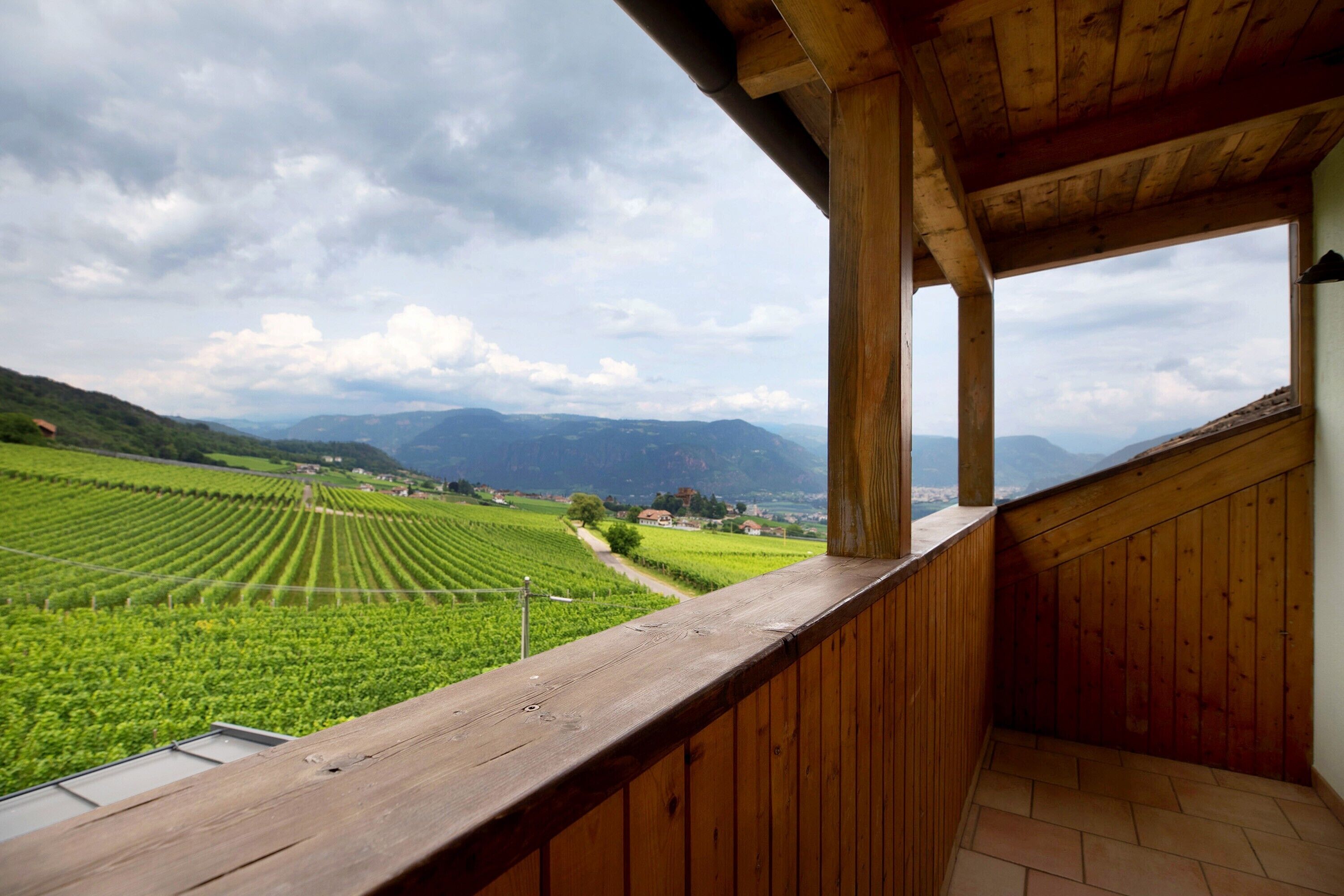 Un balcon en bois offrant une vue sur un vignoble et des montagnes lointaines.