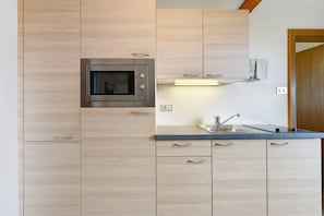 Una cocina con armarios de madera, microondas empotrado, pileta de acero inoxidable e iluminación debajo de los armarios.