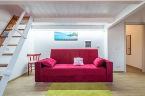 Un canapé rouge avec un coussin, une chaise en bois, un tableau et un escalier.