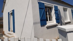 Un edificio blanco con contraventanas azules, un ventanal visible y un pequeño porche.
