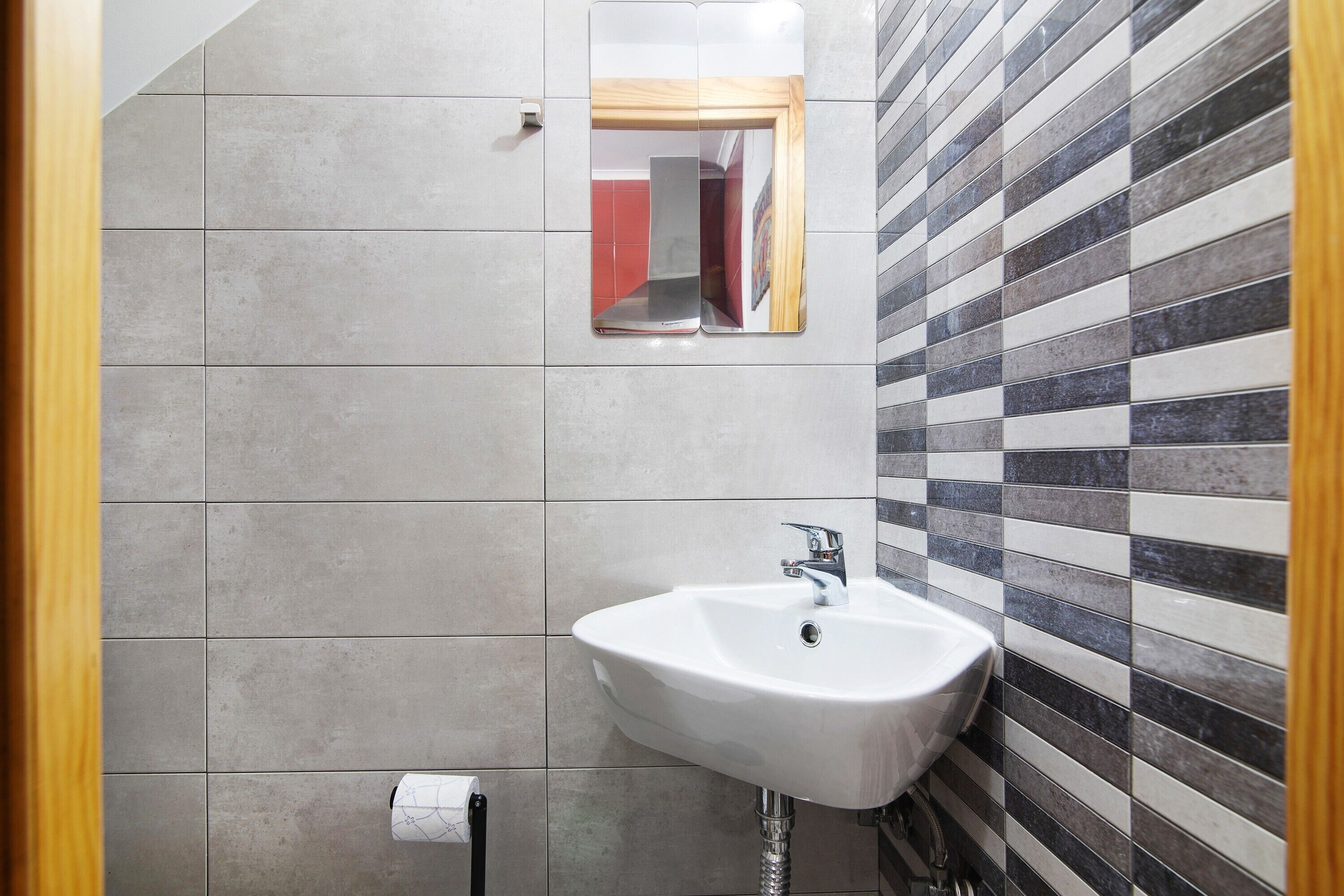 Un baño con un lavabo blanco, un espejo y una pared de azulejos a rayas.