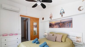 A bedroom with a bed, a dresser, a ceiling fan, a wall-mounted air conditioner, a door, and a painting. - Holiday Home 'Casa Da Avó Edite' with Private Terrace, Wi-Fi & Air Conditioning (Tavira)