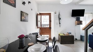 A dining area with a table set for two, a television mounted on the wall, and a staircase leading to another level. - Holiday Home 'Casa Da Avó Edite' with Private Terrace, Wi-Fi & Air Conditioning (Tavira)