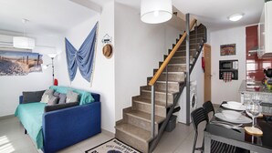 A living room with a sofa, a dining table set for two, a staircase, and a kitchen area. - Holiday Home 'Casa Da Avó Edite' with Private Terrace, Wi-Fi & Air Conditioning (Tavira)