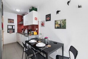 Cocina compacta con armarios blancos, salpicadero rojo y una zona de comedor con mesa y sillas negras.